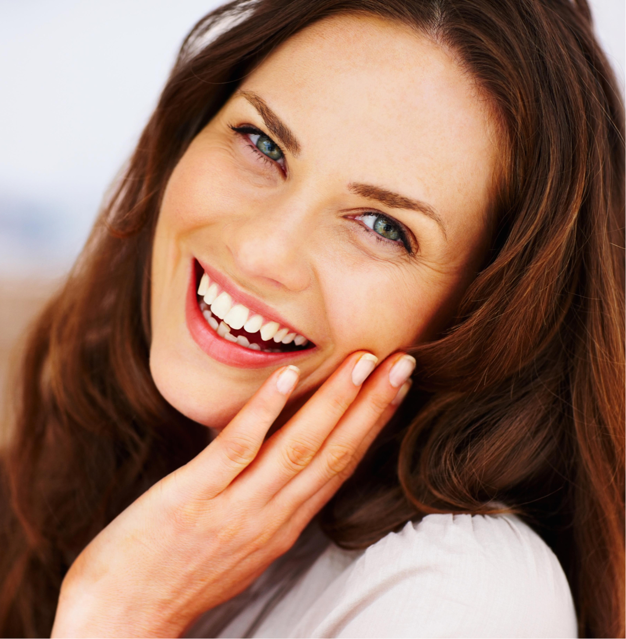 brunette model smiling and touching her face